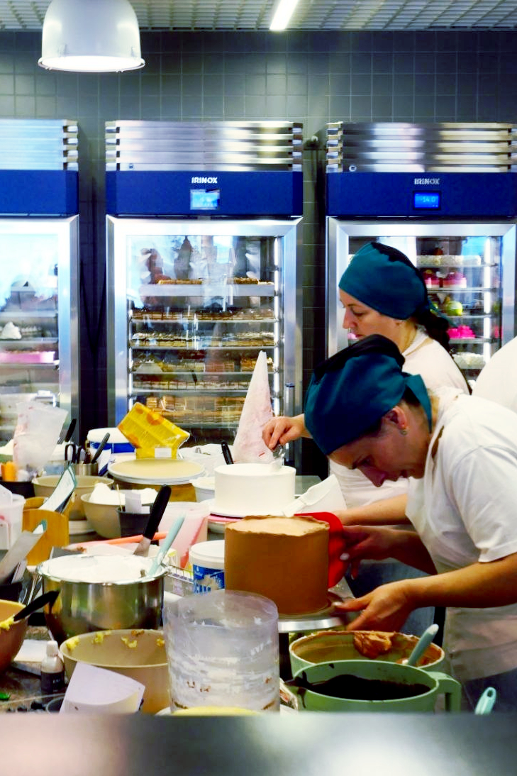 Bakers decorating cakes at a busy pastry kitchen workstation in front of Irinox chillers
